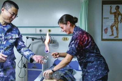 2014年7月20日，美国“仁慈”号医院船物理治疗师瑞贝尔（右）在中国和平方舟医院船中医科医生付本升的指导下学习“拔火罐”。　　□资料照片